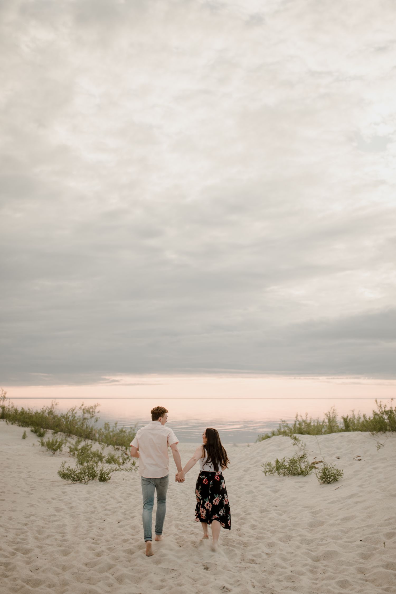 couple walking along the sand at their Grand Beach engagement session in Manitoba. Beautiful deep pink sunset, photos taken by Vanessa Renae Photography