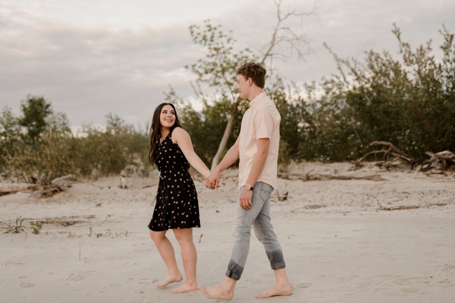 couple walking along the sand at their Grand Beach engagement session in Manitoba. Beautiful deep pink sunset, photos taken by Vanessa Renae Photography