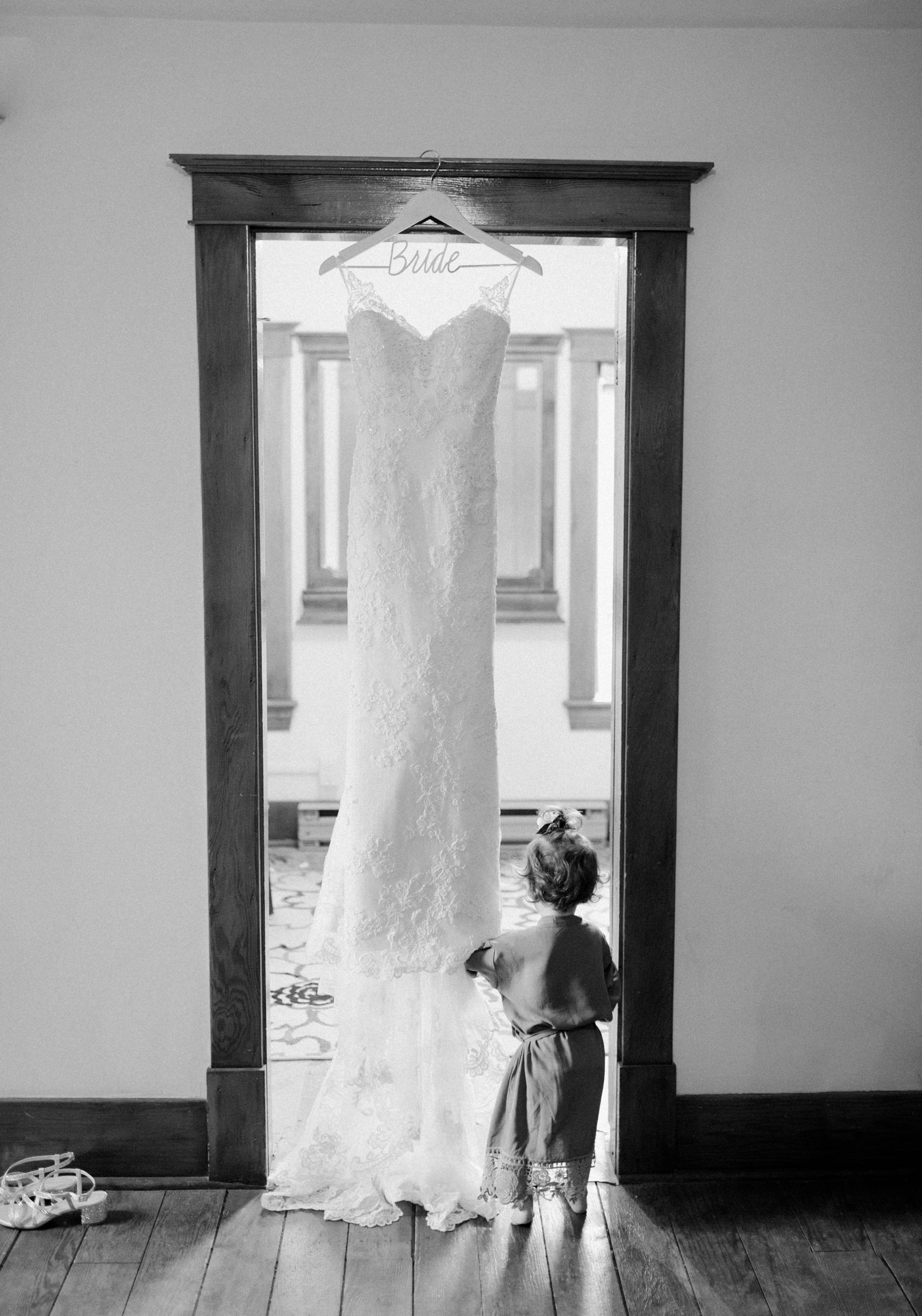 Flower girl standing by the bride's hanging dress. Shelby and Jesse celebrating their Evergreen village wedding in fall. Rustic boho wedding details. Photographed by Vanessa Renae Photography, a Winnipeg Wedding photographer